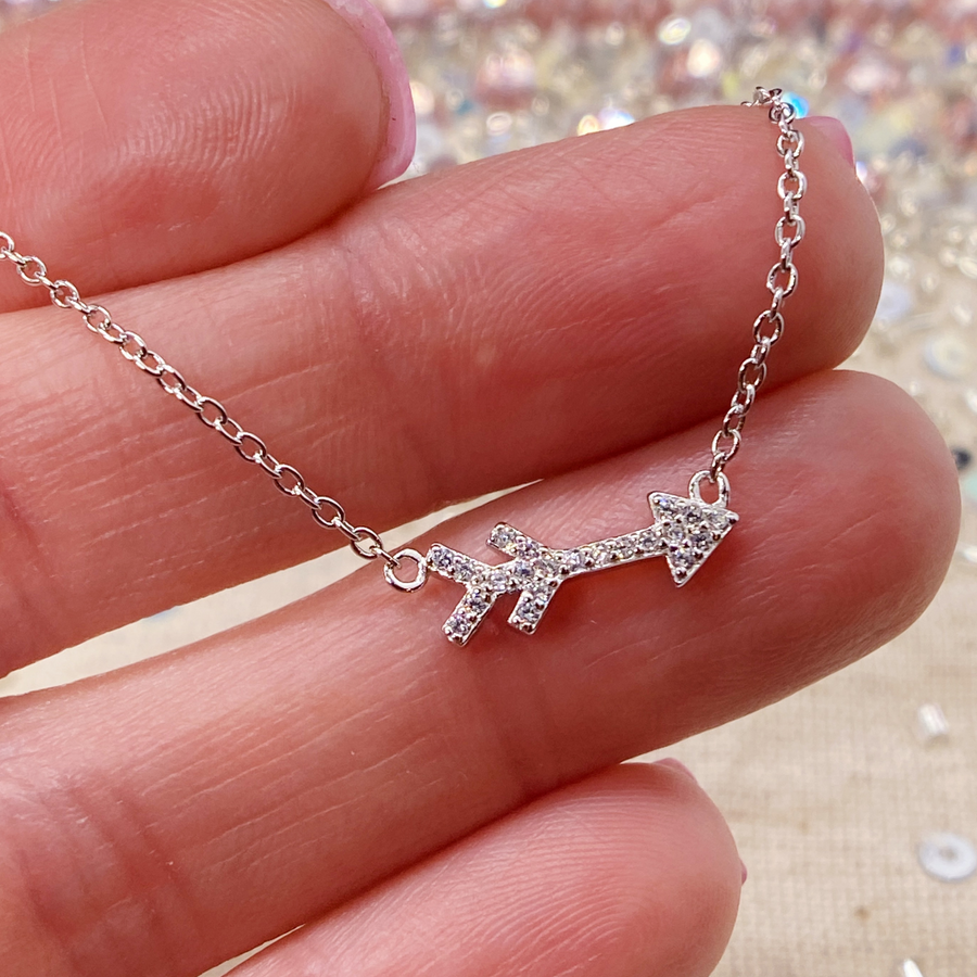 Tiny .925 Sterling Silver Arrow necklace with premium cubic zirconias in a pavé setting, held in hand for scale.