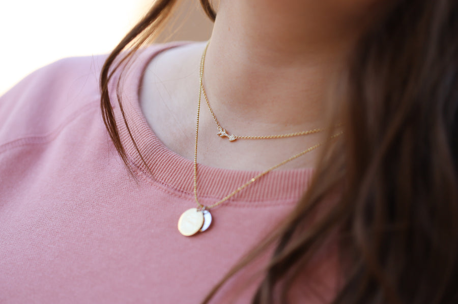 Model wearing Tiny Arrow .925 silver necklace Tiny Arrow .925 silver necklace with premium cubic zirconias in a pavé setting, layered with charm necklace. 